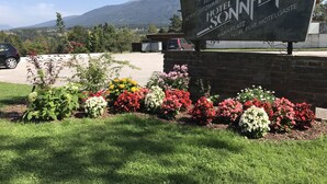 Une enseigne d’hôtel indiquant les équipements disponibles, entourée d’un jardin aménagé avec différentes variétés de fleurs.