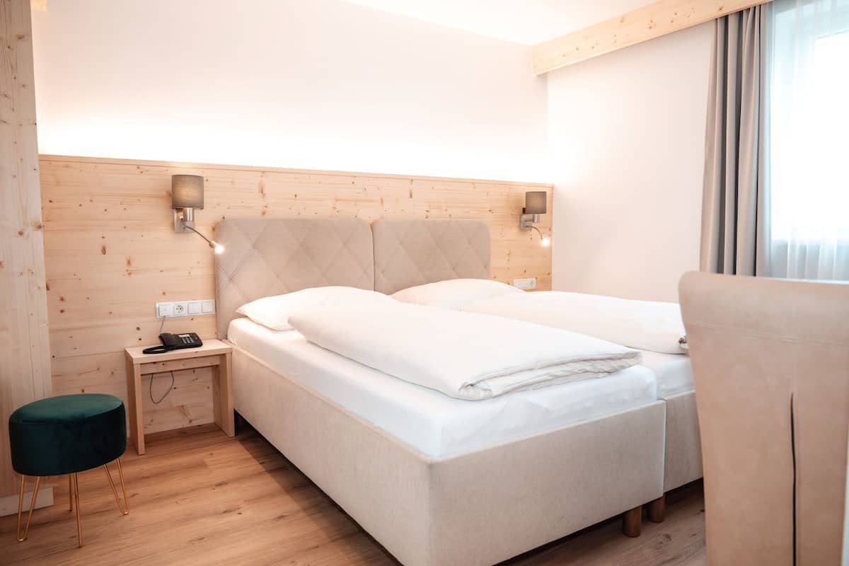 Habitación de hotel con cabecera de madera, mesita de noche con teléfono, taburete verde y cama con ropa blanca.
