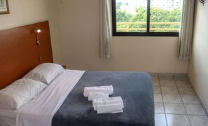 A hotel room with a bed, a headboard, a window with curtains, and a view of greenery outside. - Ameris Hotel Vila Rica Flat (Resende)