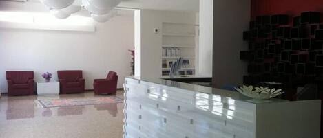 A reception area with a modern design, featuring a reception desk, seating area with chairs, and a wall with storage units.