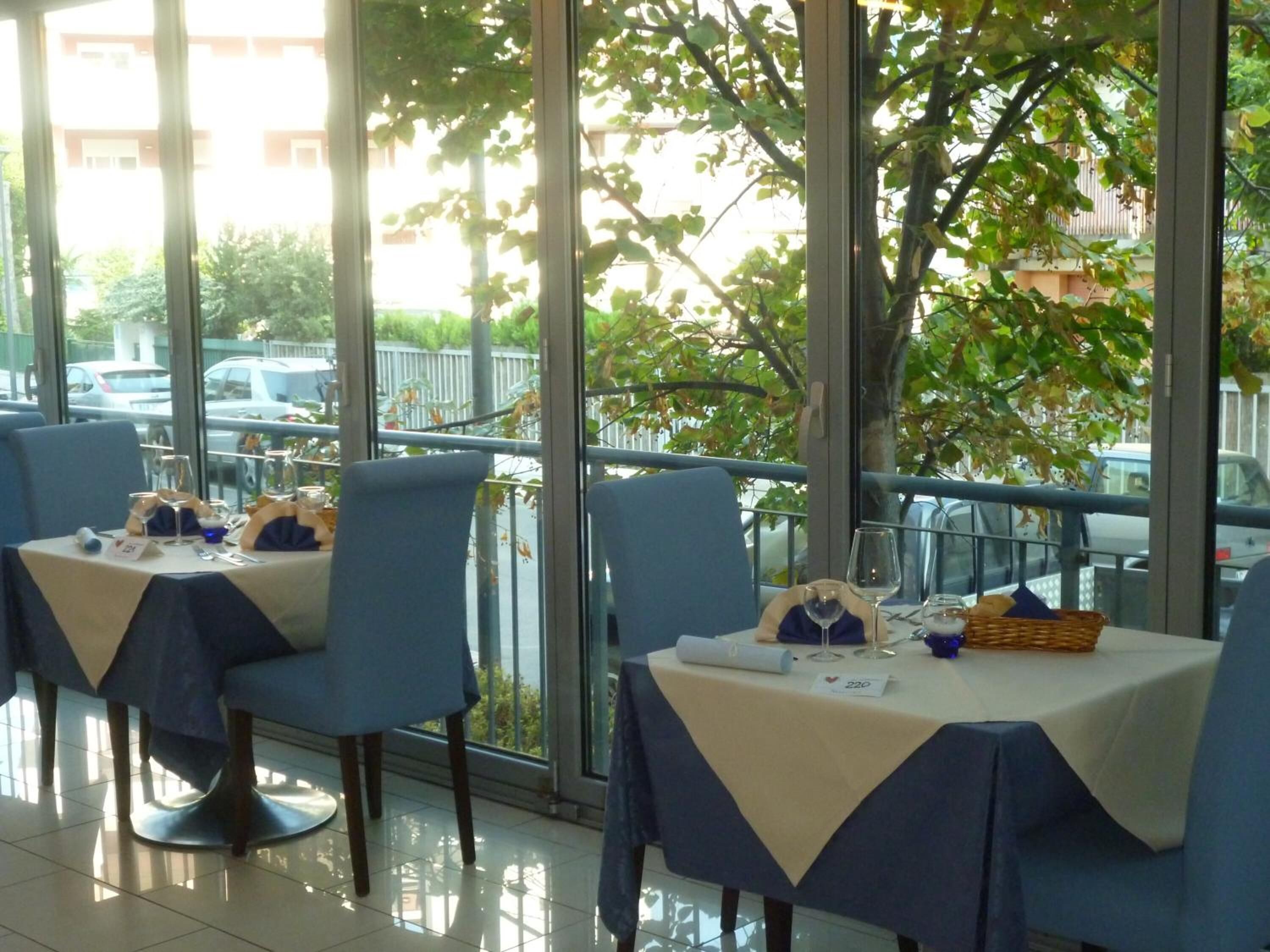 A restaurant with tables set for dining, large windows, and a view of the street.