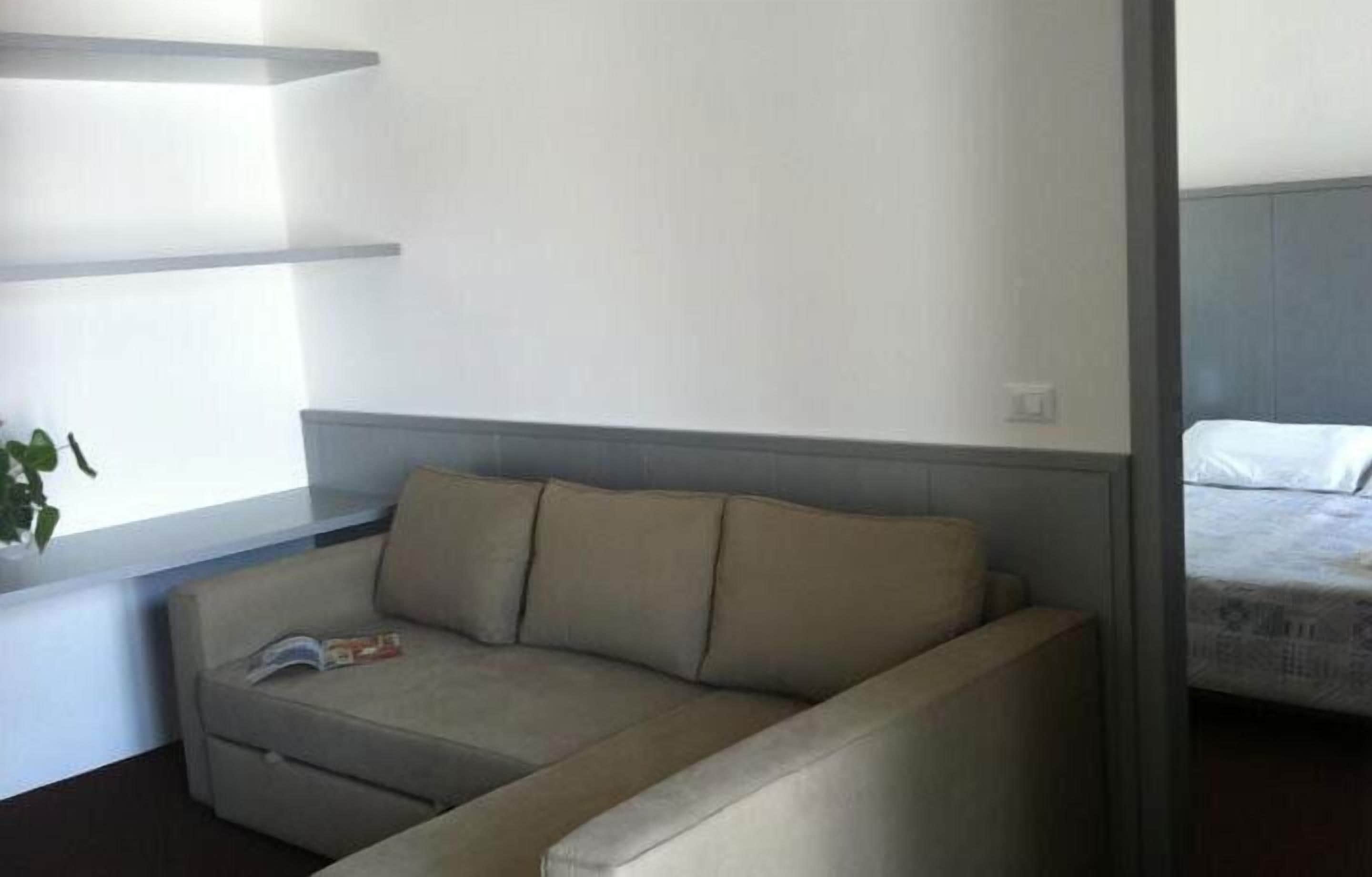 A room with a sofa, a bed, and a window with a plant.