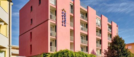 Un edificio hotelero rosa con balcones, un letrero que dice "EURO HOTEL" y un cartel para "J.F. Kennedy" cerca.