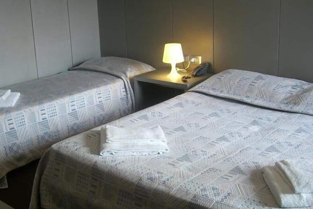 A hotel room with two single beds, each with a patterned bedspread and pillows, a bedside table with a lamp, and a telephone.