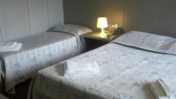 A hotel room with two single beds, each with a patterned bedspread and pillows, a bedside table with a lamp, and a telephone.