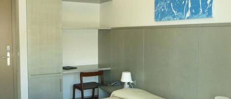 Habitación de hotel con cama, escritorio, silla y estante en la pared.