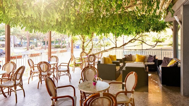 An outdoor seating area with wicker furniture and a view of the street. - Hotel Europa (Grado)