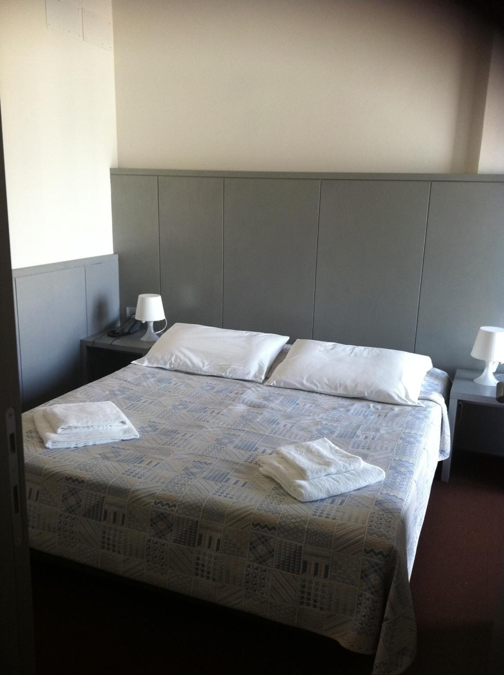 A hotel room with a bed, two bedside tables, and a headboard.