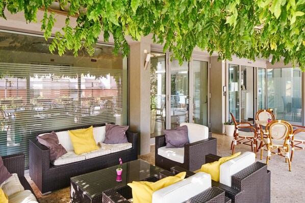 Un área de estar exterior moderna con mobiliario de mimbre y puertas de vidrio que dan a un espacio interior.