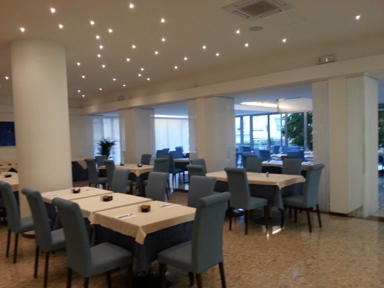 Un comedor amplio con varias mesas y sillas, ventanas grandes y un diseño de techo moderno.