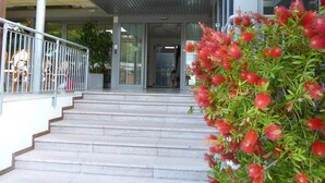 A staircase leading to a building entrance with a metal railing and a bush with red flowers. - Hotel Europa (Grado)