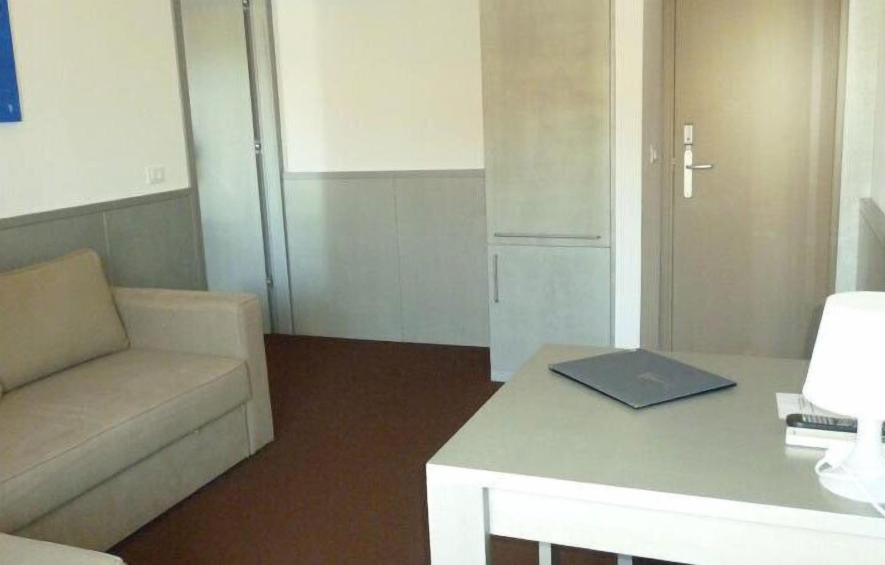 Una habitación pequeña y sencilla, con una mesa blanca, un sofá color beige y una puerta.