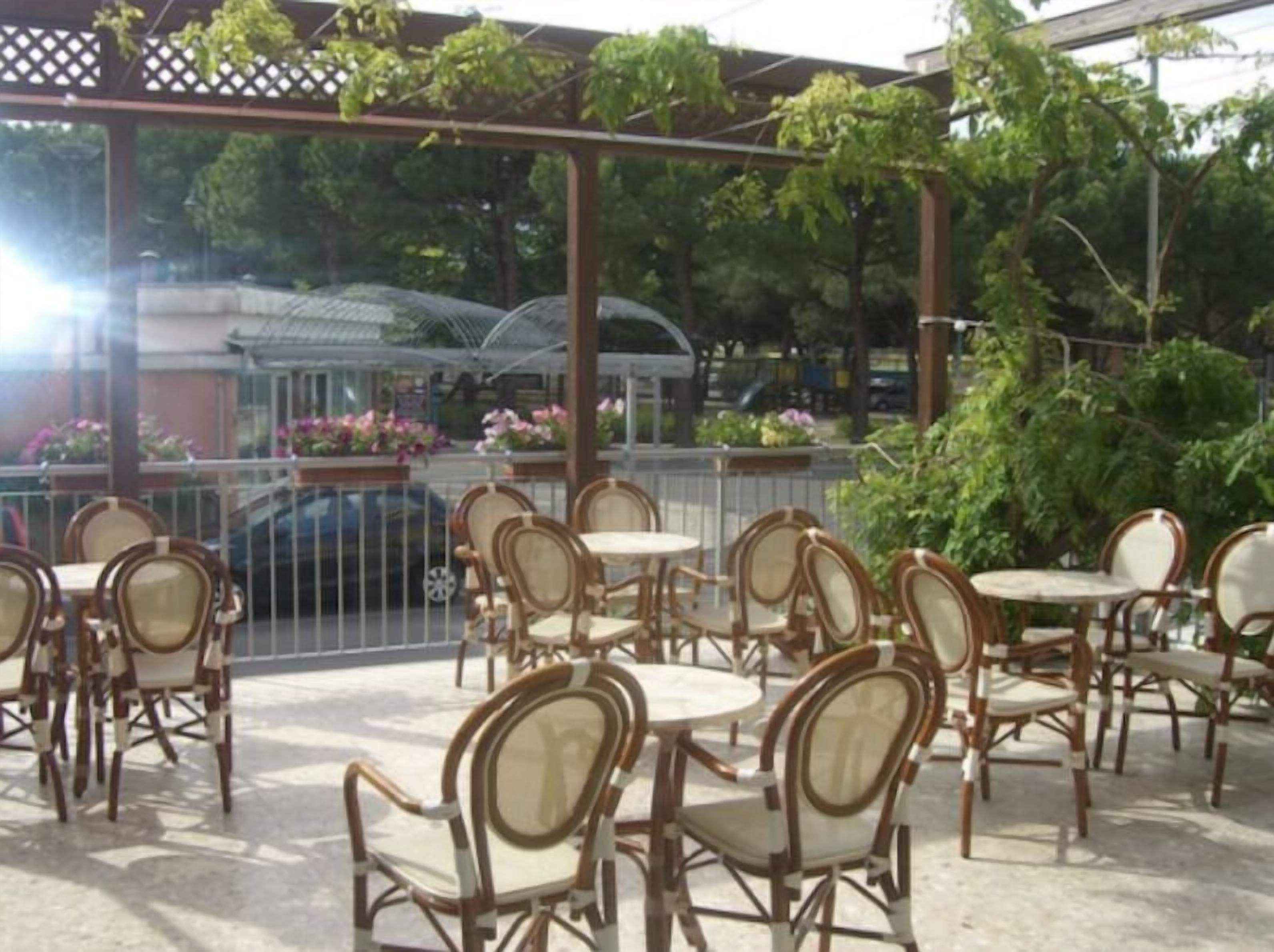 Un patio al aire libre con sillas de mimbre y mesas redondas, rodeado por una valla de metal y follaje.