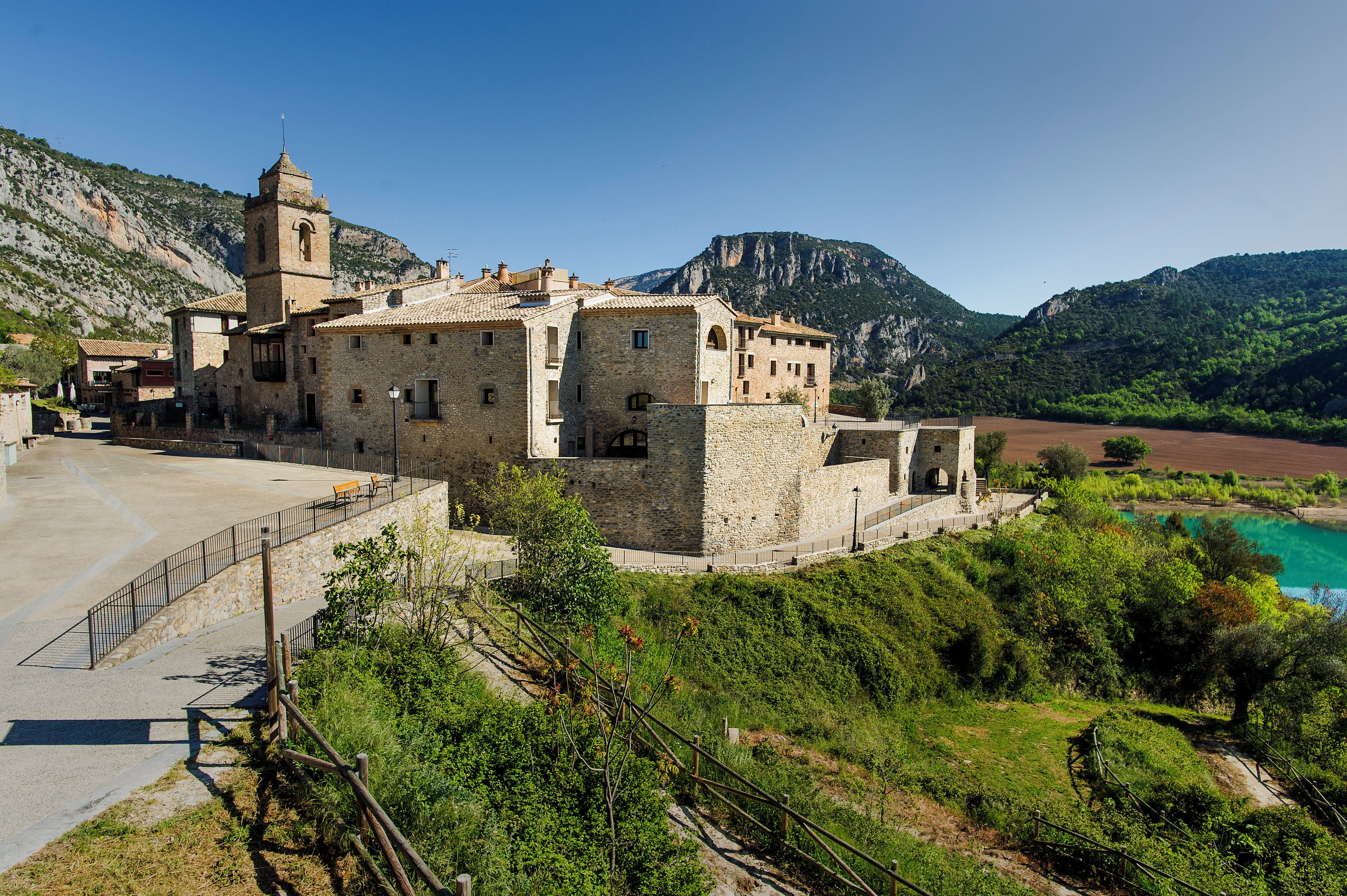 A historic stone building with a bell tower, situated on a hillside overlooking a valley.