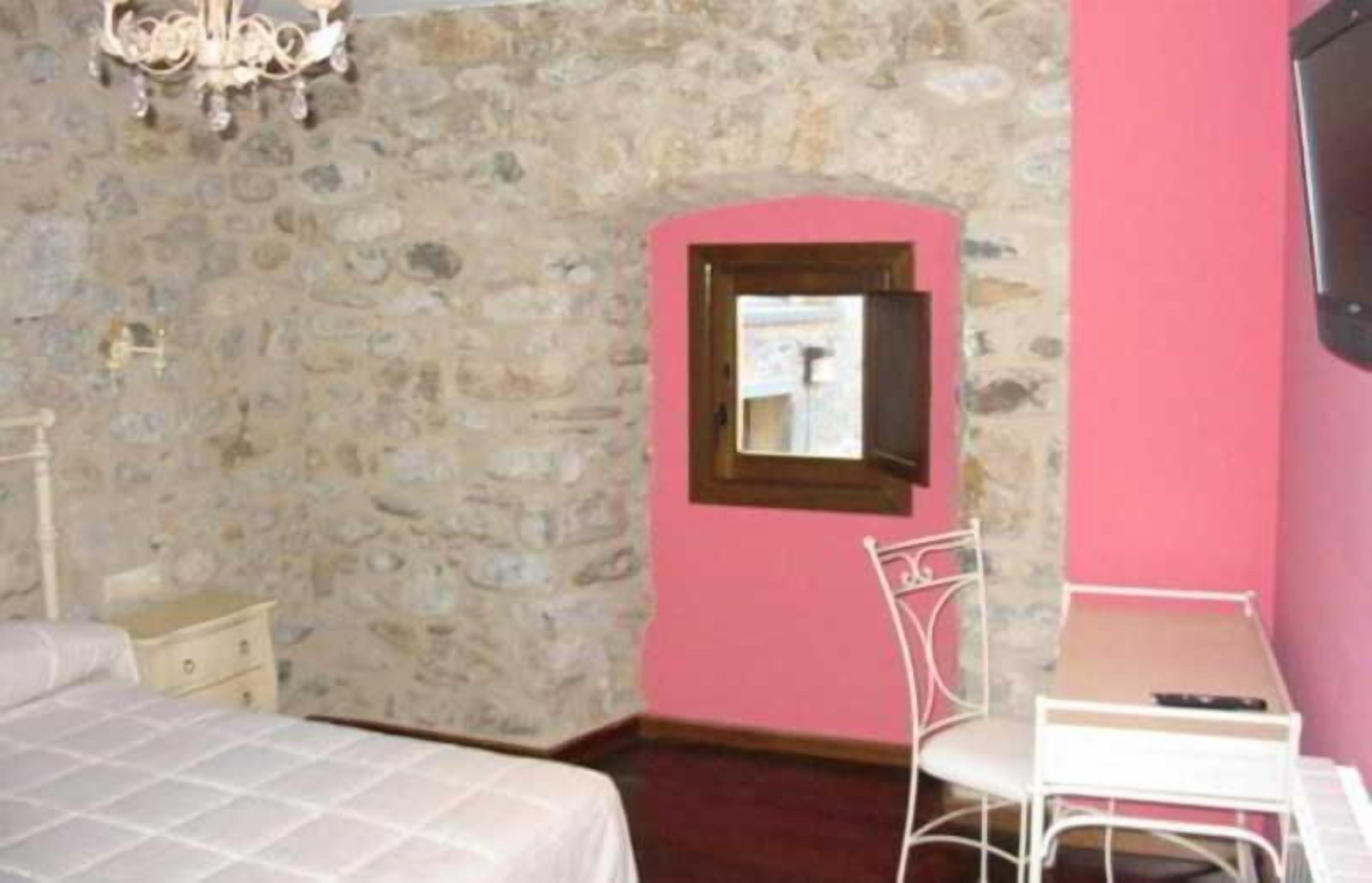 A room with a stone wall, a bed, a desk with a chair, and a small window.