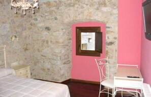 Une pièce avec un mur en pierre, un lit, un bureau avec une chaise et une petite fenêtre.