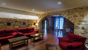 A cozy room with a stone wall, red sofas, and a dining area with chairs and a table. - Ligueerre Resort (Abizanda)