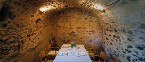 Un comedor con pared de piedra, una mesa dispuesta para dos personas y dos sillas.