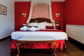 A neatly made bed with white linens and a red bedspread, a wooden bench at the foot of the bed, and a red wall with a white radiator. - Ligueerre Resort (Abizanda)