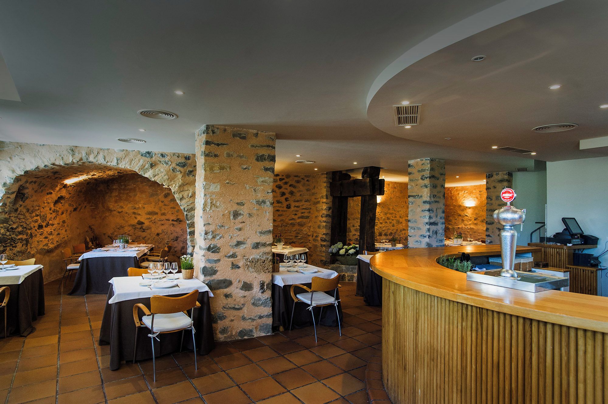 A restaurant with stone walls, wooden tables, and a bar area.