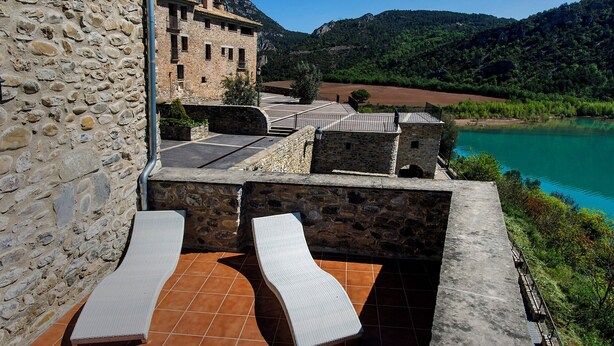 A stone building with a terrace featuring two lounge chairs and a view of a lake and mountains. - Ligueerre Resort (Abizanda)