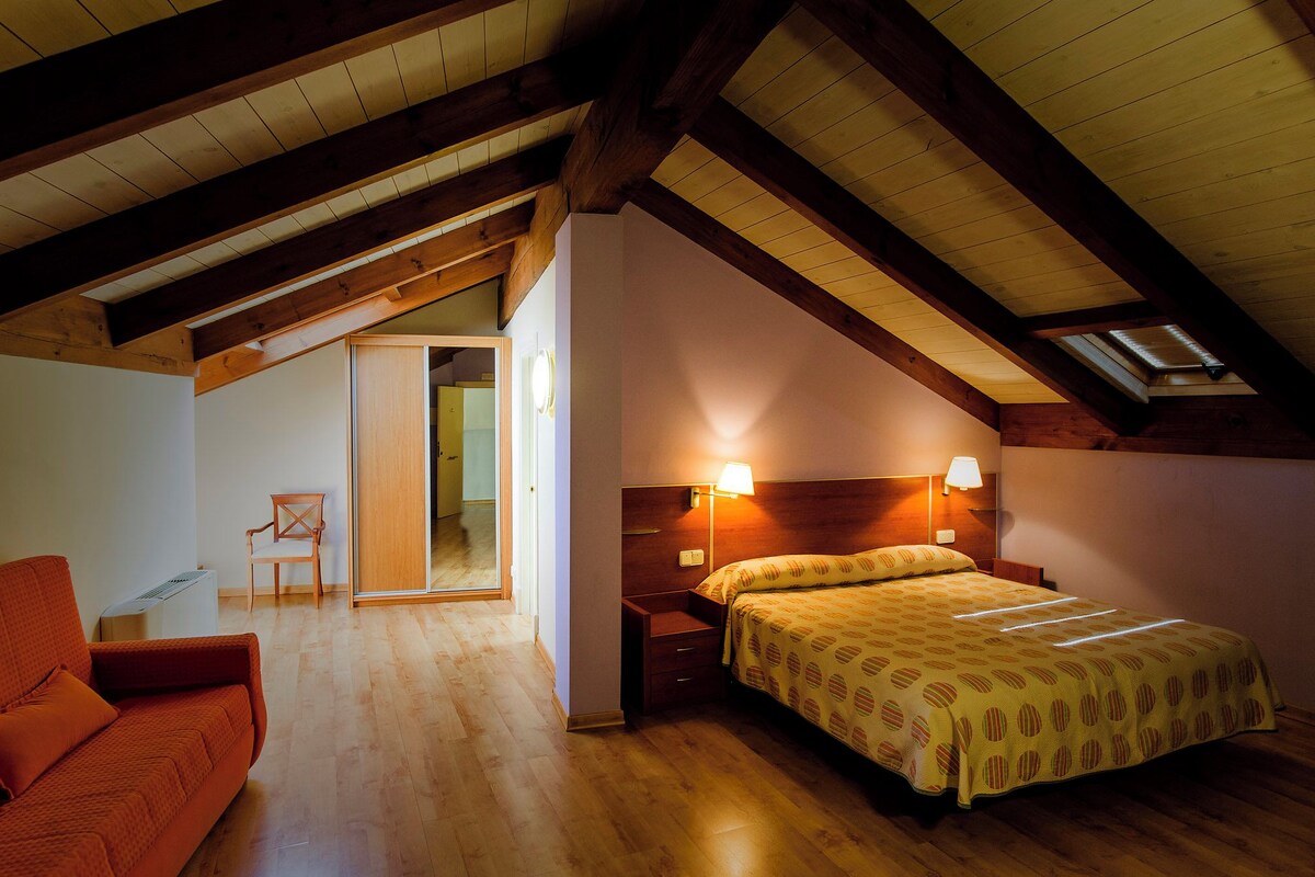 A bedroom with a wooden ceiling, a bed with patterned bedding, a nightstand, and a chair.