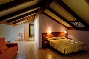 A bedroom with a wooden ceiling, a bed with patterned bedding, a nightstand, and a chair.