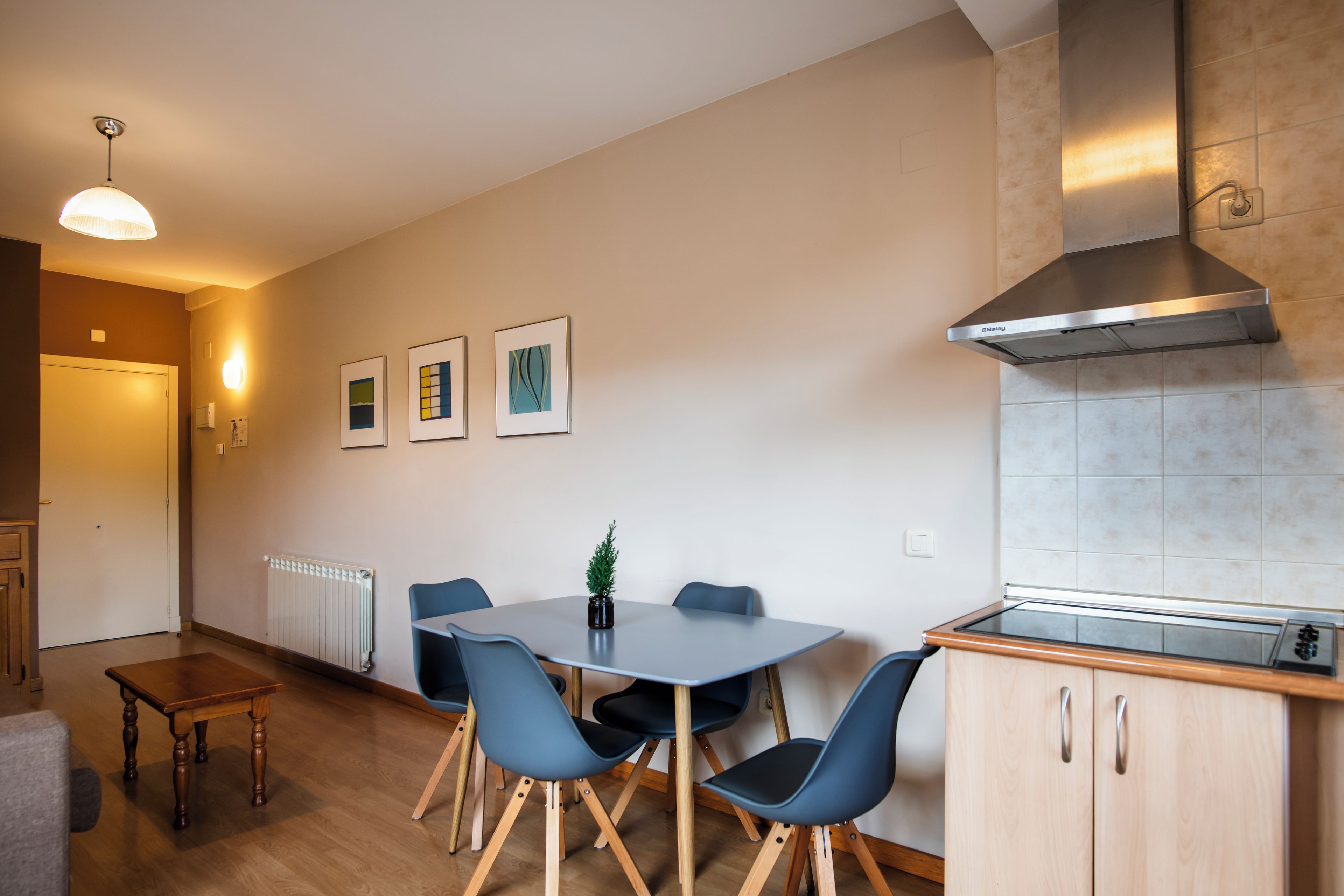 Una cocina moderna con estufa integrada, campana de acero inoxidable y un comedor con mesa y sillas.