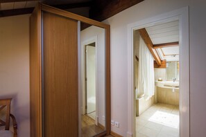 Une chambre avec une armoire en bois, un miroir et une salle de bain équipée d’un lavabo et d’une douche.