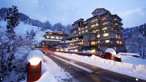 A multi-story hotel with a snow-covered landscape, a road with vehicles, and a lit entrance. - Yomogihira Onsen Izumiya (Nagaoka)
