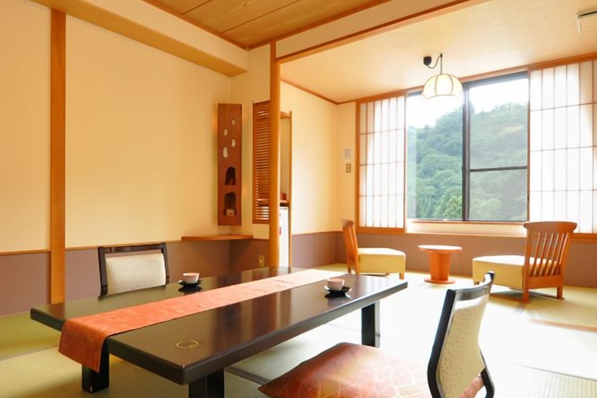 A tatami mat room with a low table, chairs, and a view of the outdoors.