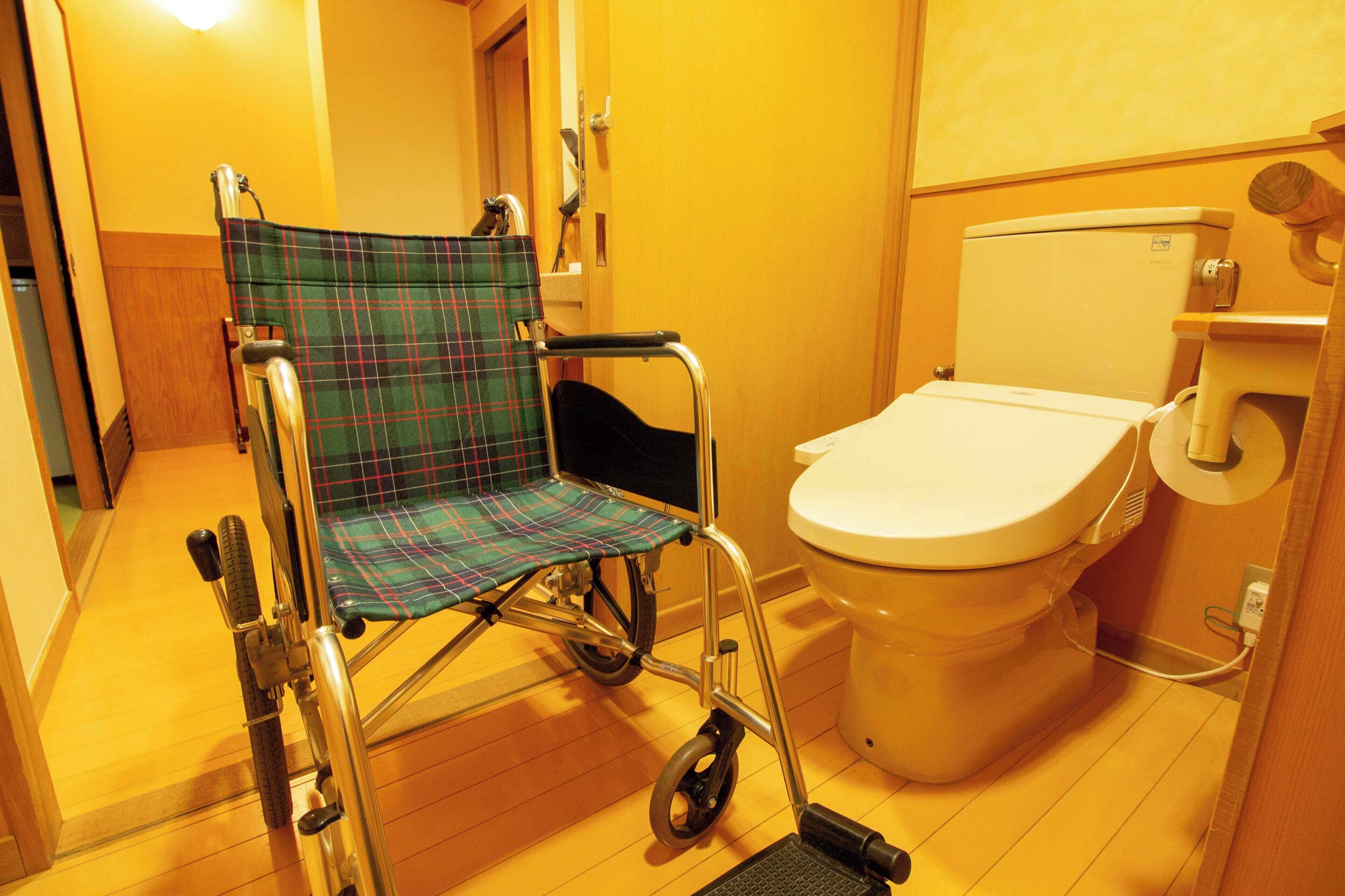 A wheelchair in a bathroom with a toilet and a wooden floor.