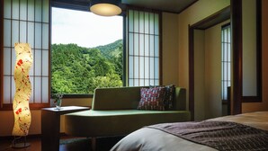 A bedroom with a bed, a sofa, a table with a vase, and a view of a forest through large windows. - Yomogihira Onsen Izumiya (Nagaoka)