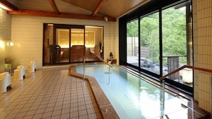 A spa area with a tiled floor, a pool, and a large window offering a view of greenery. - Yomogihira Onsen Izumiya (Nagaoka)