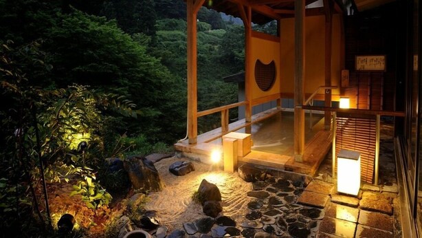 A wooden structure with a stone pathway leading to a covered area, surrounded by dense forest. - Yomogihira Onsen Izumiya (Nagaoka)