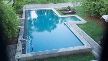 Una piscina rectangular con borde de azulejos, rodeada de césped y una pequeña terraza con sillas de descanso.