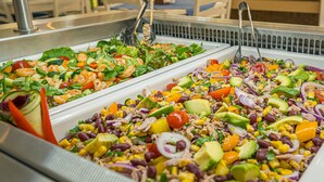 En buffet med forskellige salater og et siddeområde med borde og stole.