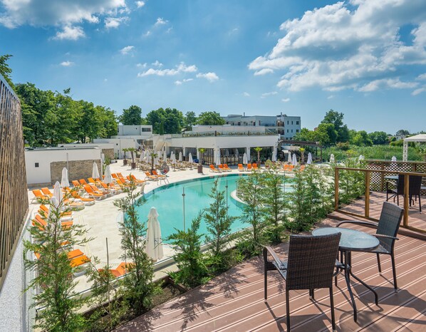 A pool area with orange lounge chairs and umbrellas, surrounded by greenery and a building in the background. - Mera Resort Venus (Venus)