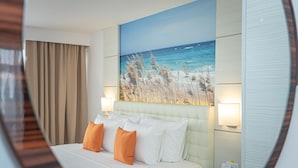 Et hotelværelse med en seng, to sengeborde, to læselamper og et maleri af en strand.