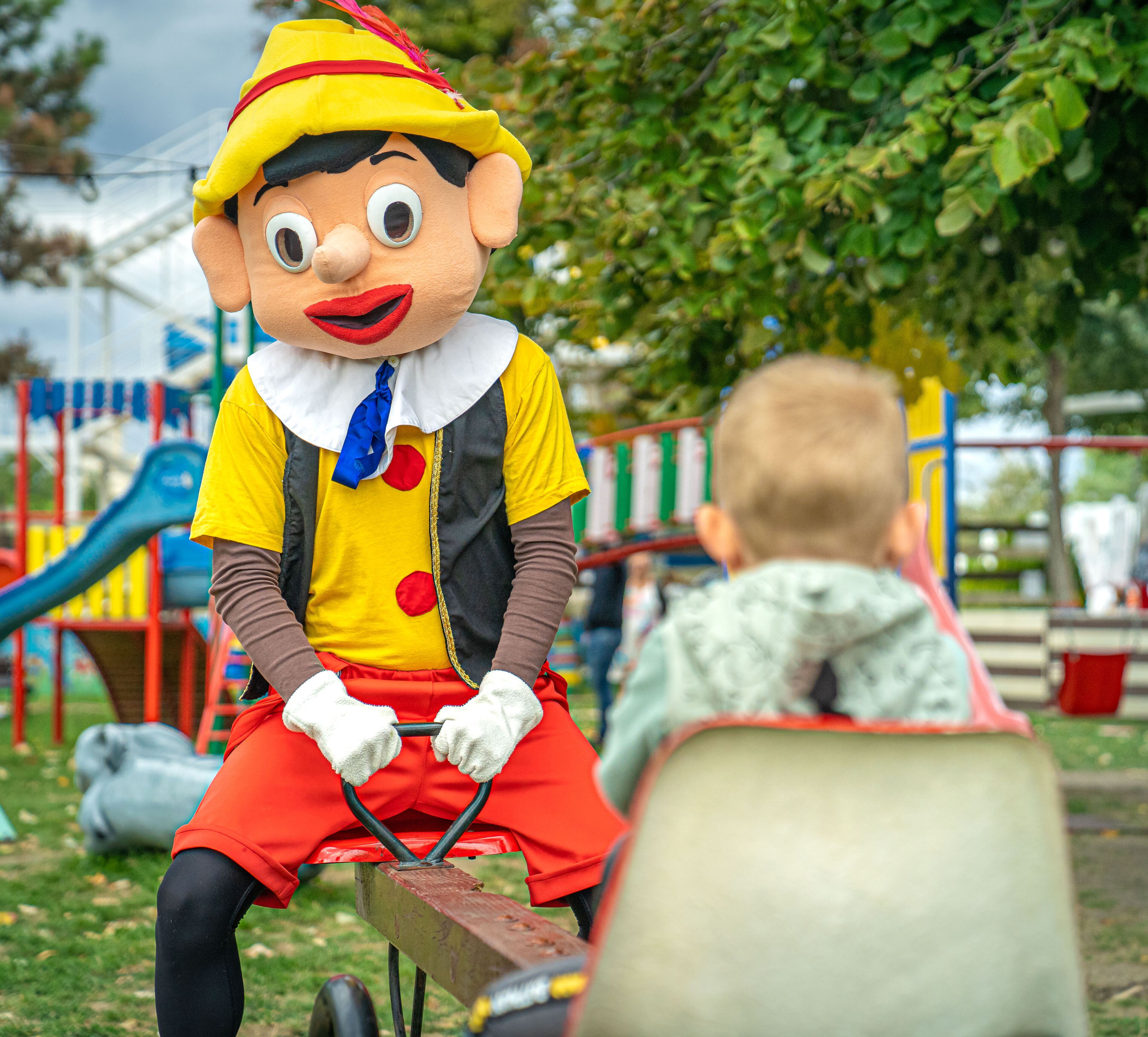 A person in a yellow hat and red outfit sitting on a bench in a park.