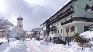 Una calle nevada con edificios, incluido un hotel llamado "Hotel Pension Kirchplatz".