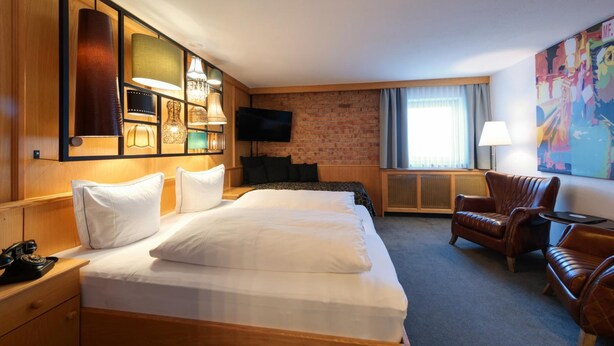 Una habitación de hotel con una cama grande, televisión, pared de ladrillo y una ventana con cortinas.