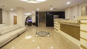 Et hotel lobby med en reception, en sofa, en tæppe med mønster, og en trappe til et andet område.