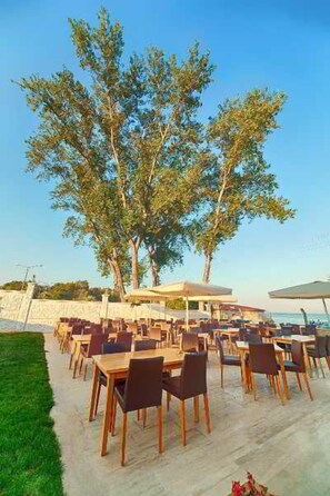 An outdoor dining area with tables and chairs, surrounded by trees and a view of the sea. - Hamzakoy Bluepark Boutique Hotel (Gallipoli)