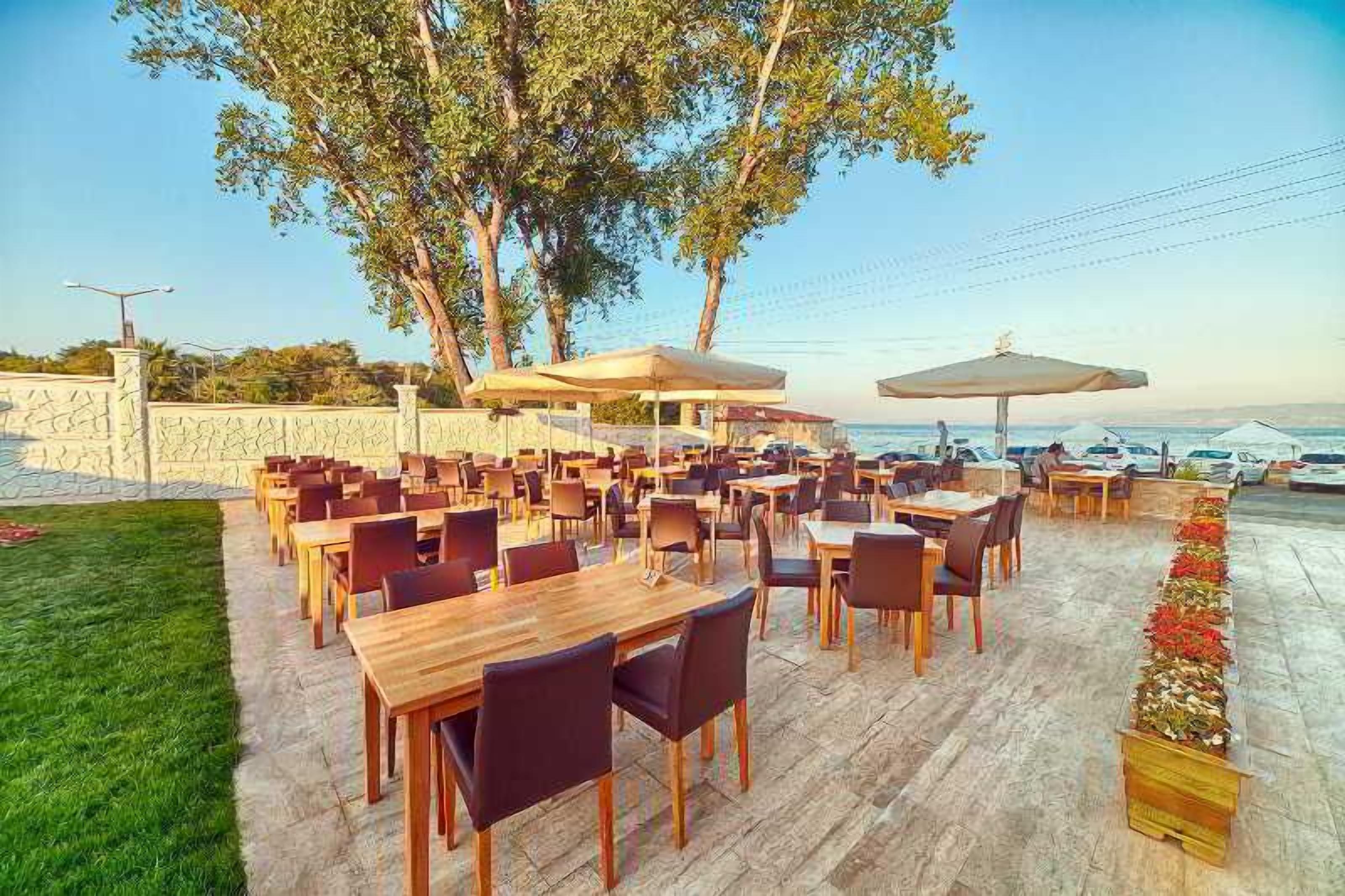 Un espacio de comedor al aire libre con mesas y sillas de madera, sombrillas y vista al océano.