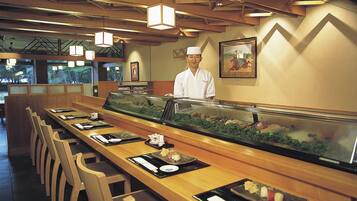 A sushi bar with a chef, wooden tables, and a fish tank display.