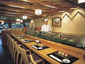 A sushi bar with a chef, wooden tables, and a fish tank display. - Hokkaido Hotel (Obihiro)
