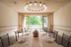 A conference room with a long table set for a meeting, large windows with a view of greenery, and a modern chandelier. - Hokkaido Hotel (Obihiro)