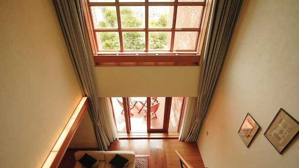 A spacious living area with a high ceiling, a wooden staircase, and a view of the outdoors through large windows. - Hokkaido Hotel (Obihiro)