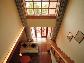 A spacious living area with a high ceiling, a wooden staircase, and a view of the outdoors through large windows. - Hokkaido Hotel (Obihiro)